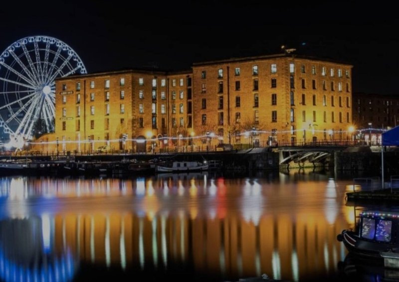 Waterfront brick building at night with illuminated facade, ferris wheel, and water reflections