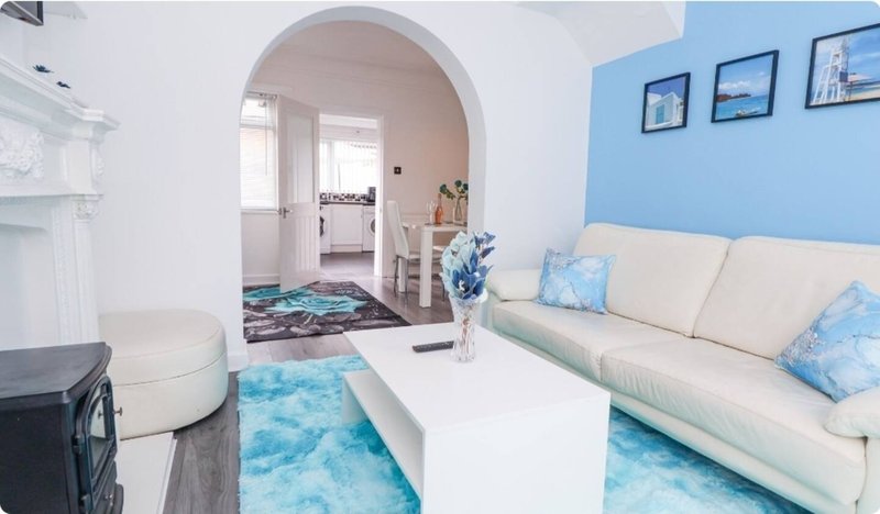 Bright living room with cream sofa, blue accent wall, white coffee table and archway to kitchen