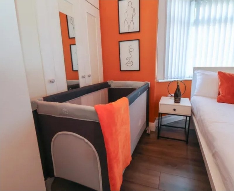 Bedroom with double bed, travel cot, orange accent wall and bedside table
