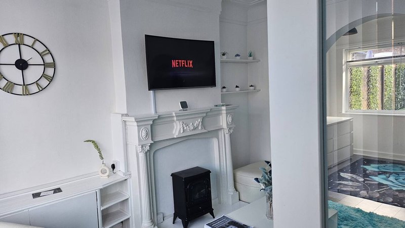 Living room with fireplace, wall-mounted TV, clock, shelving and window with garden view
