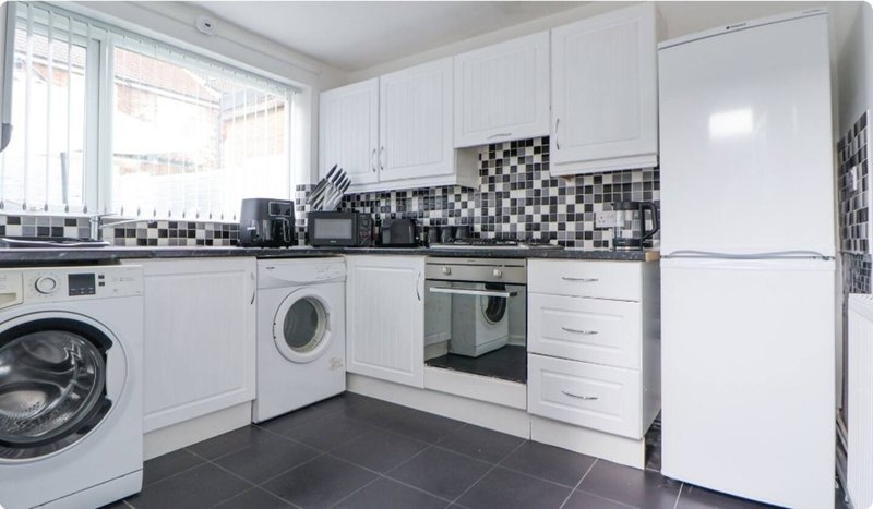 Modern kitchen with white cabinetry, black and white tile backsplash, appliances and washing machine