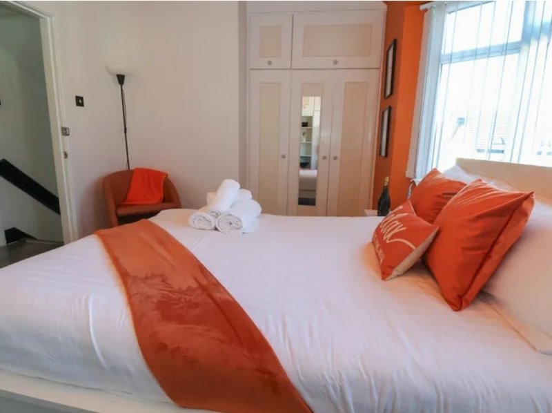 Bright bedroom with double bed, orange accent pillows, white towels, and built-in wardrobe