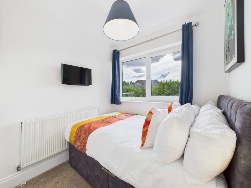 Bright bedroom with double bed, white pillows, pendant lamp, wall-mounted TV and garden view