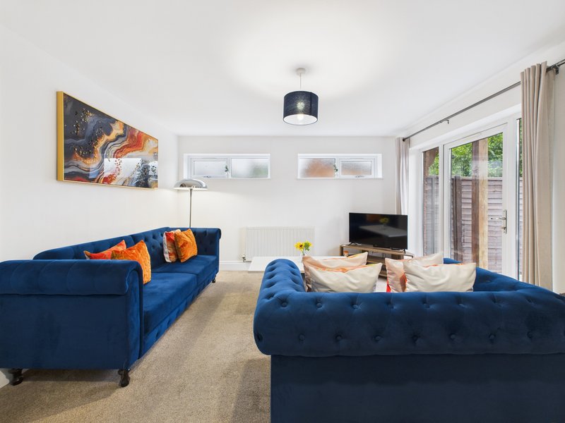 Modern living room with two blue sofas, TV, artwork, and glass doors to garden
