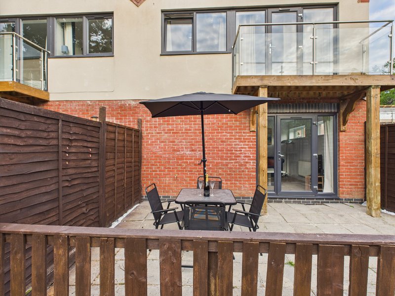 Brick patio with dining table, chairs, black umbrella and wooden fence