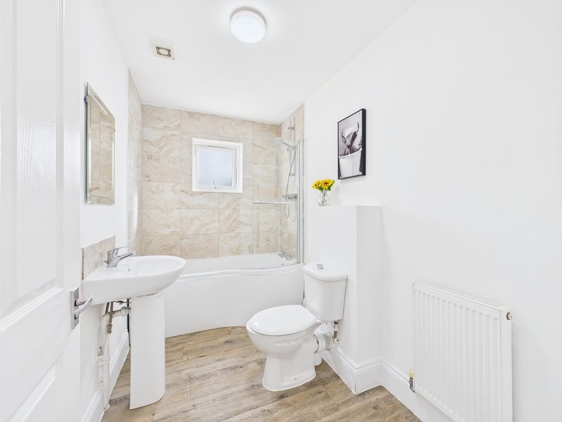 Modern bathroom with white suite, curved bath, beige tile walls and wooden floor