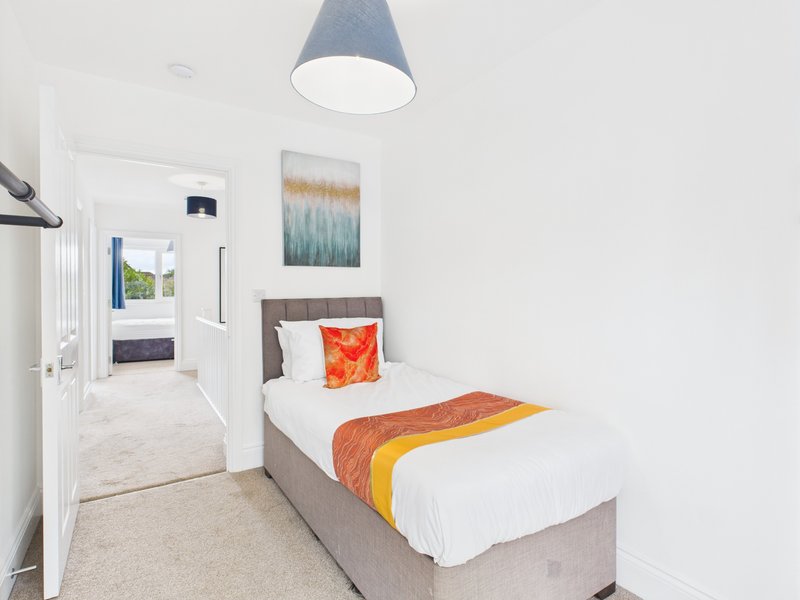 Bright bedroom with single bed, pendant lamp, abstract wall art, and view to hallway