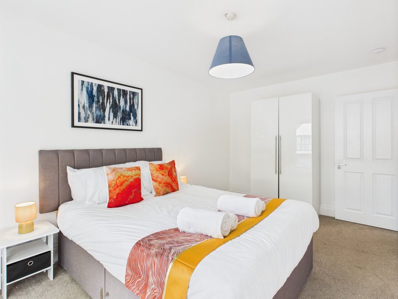 Bright modern bedroom with grey upholstered bed, white bedding, colorful cushions and throw blanket