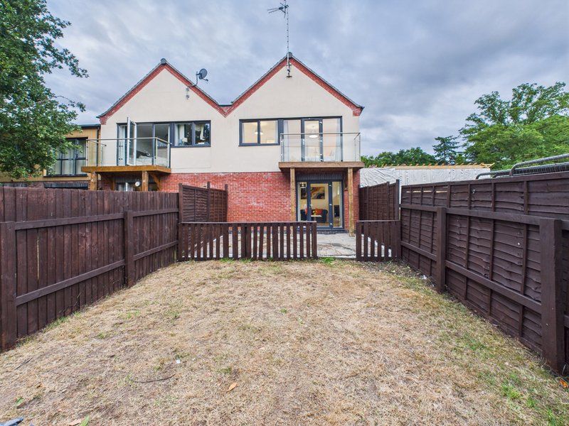Modern two-storey house with brick base, cream upper storey, fenced gravel courtyard and wooden decking entrance