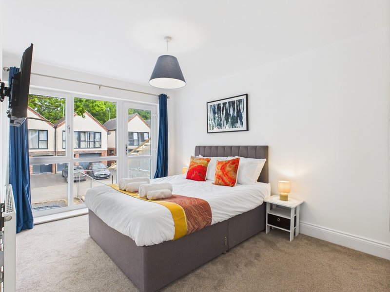 Bright bedroom with double bed, colorful pillows, pendant lamp, and glass doors to patio
