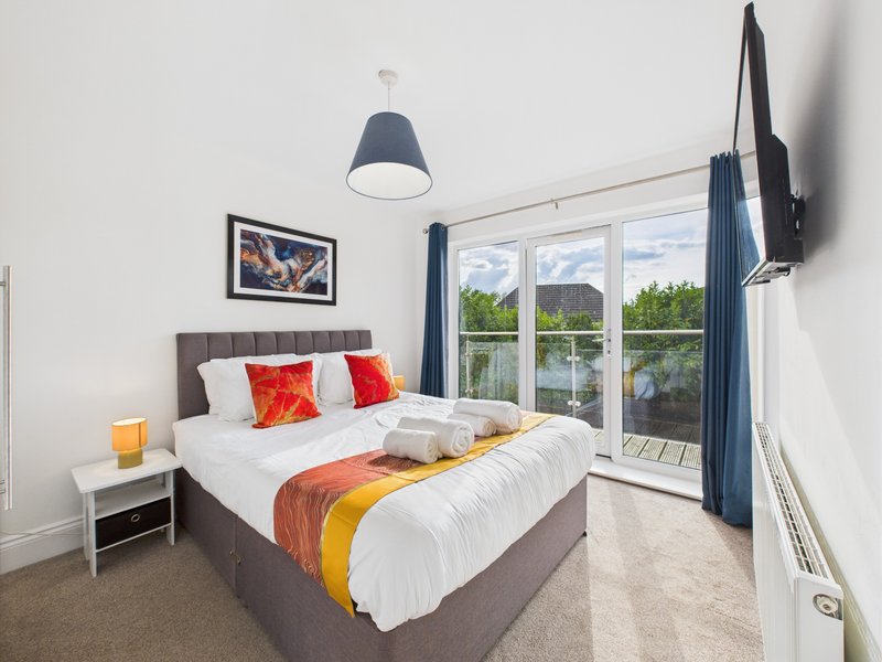 Modern bedroom with double bed, colorful pillows, pendant lamp and large window overlooking trees