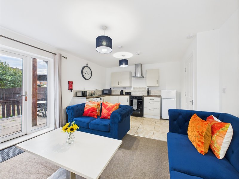 Open-plan living room with blue sofas, kitchen area, white coffee table and garden access