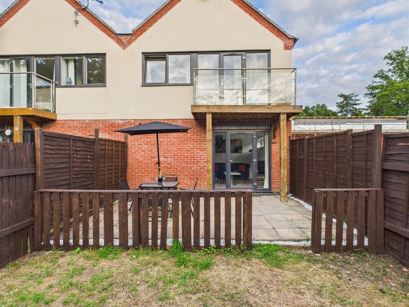 Modern brick and cream render house exterior with wooden deck, fencing and patio area