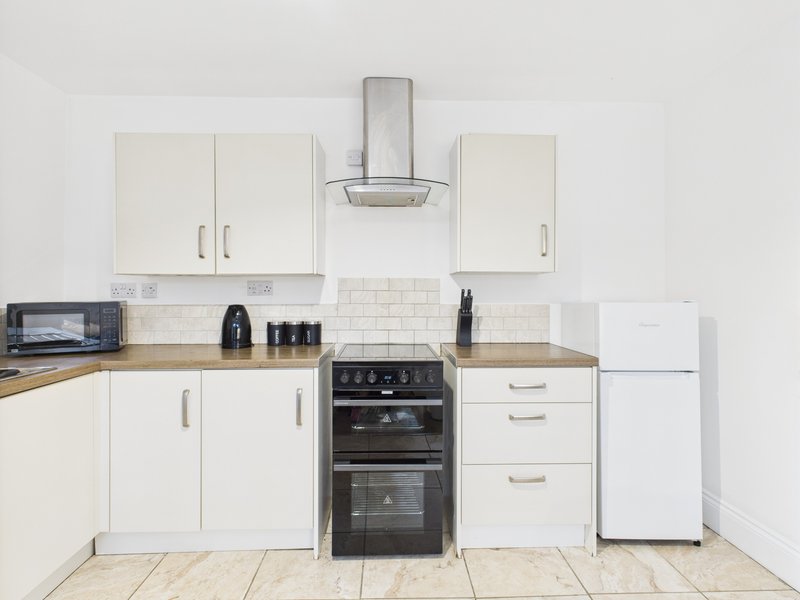 Modern kitchen with white cabinets, black double oven, stainless steel cooker hood and tiled floor