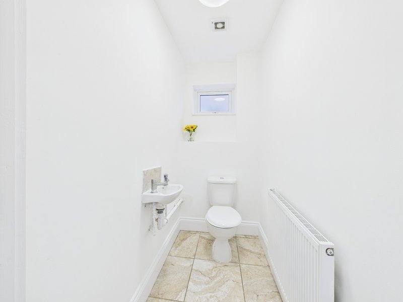 Clean white bathroom with toilet, wall-mounted sink, small window and tiled floor