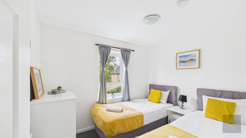 Bright twin bedroom with two single beds, yellow bedding, white furniture and window with garden view