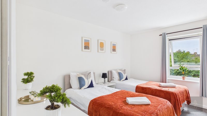 Bright bedroom with two single beds, orange throws, blue cushions and garden view