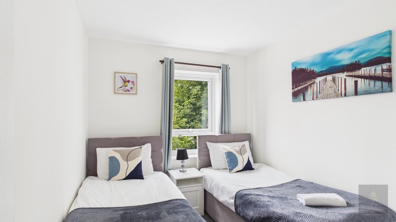 Twin bedroom with two single beds, grey headboards, blue and white cushions, window with garden view