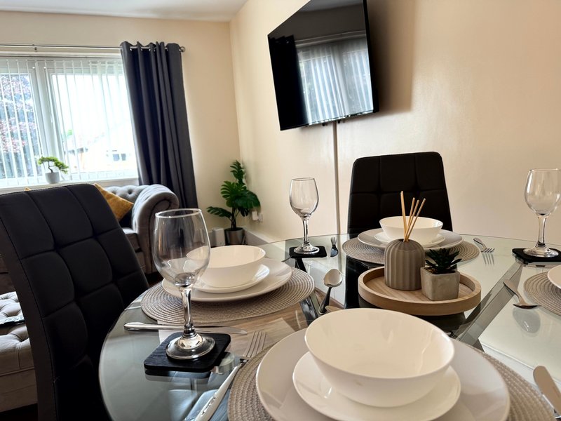 Dining area with set table, black chairs, wall-mounted TV, and windows with curtains