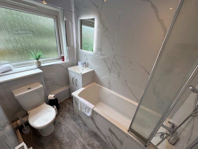 Modern bathroom with toilet, sink, bath and shower enclosure, marble tiles