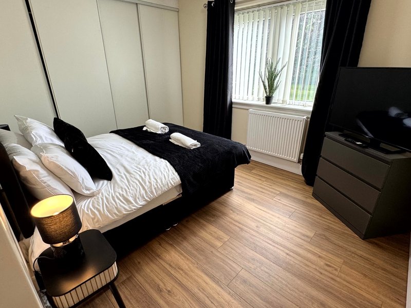 Modern bedroom with black four-poster bed, white bedding, wooden floor, TV, and window with black curtains