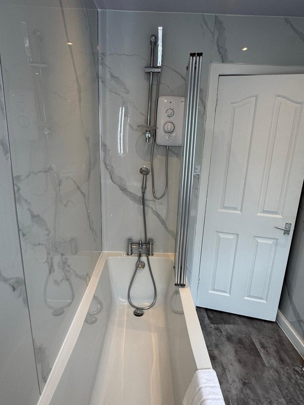 Modern bathroom with white bathtub, chrome shower fixtures, marble-effect tiling, and white door
