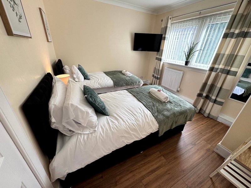 Bedroom with double bed, grey and white bedding, wall-mounted TV, and windows with curtains