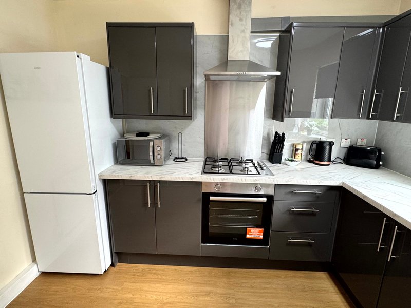 Modern kitchen with white fridge, black cabinetry, gas hob, oven and wooden flooring