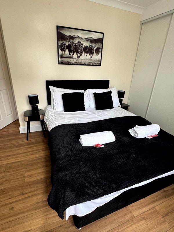 Modern bedroom with black and white bedding, wooden floor, framed wall art, and bedside tables
