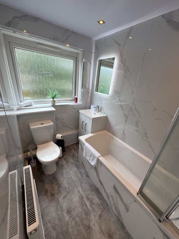 Modern bathroom with toilet, sink, bathtub, shower screen, and window overlooking garden