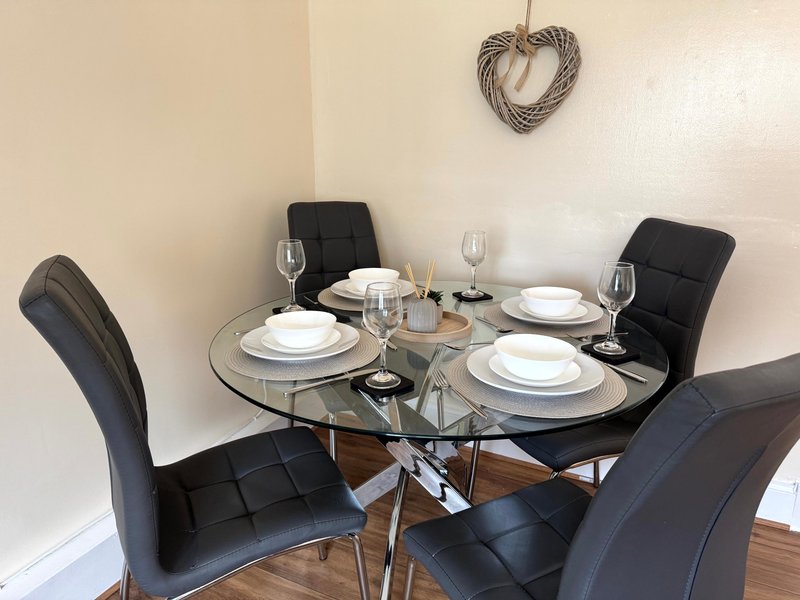 Dining table set for four with black chairs, place settings, and glasses