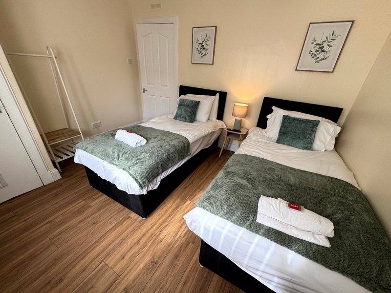 Twin bedroom with two single beds, green bedding, wooden floor and botanical wall art