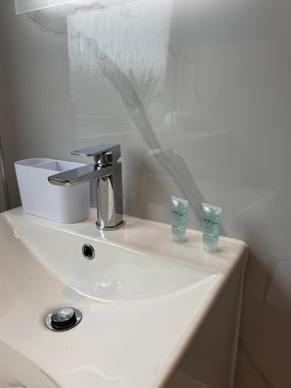 Modern bathroom sink with chrome faucet, white soap dispenser, small toiletries bottles, and shower curtain