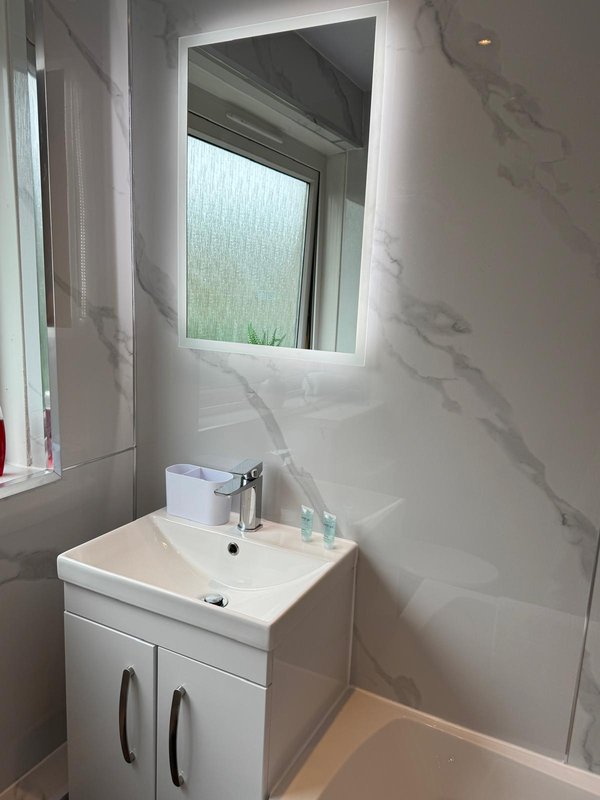 Modern bathroom with white vanity sink, illuminated mirror, and marble-effect wall tiles
