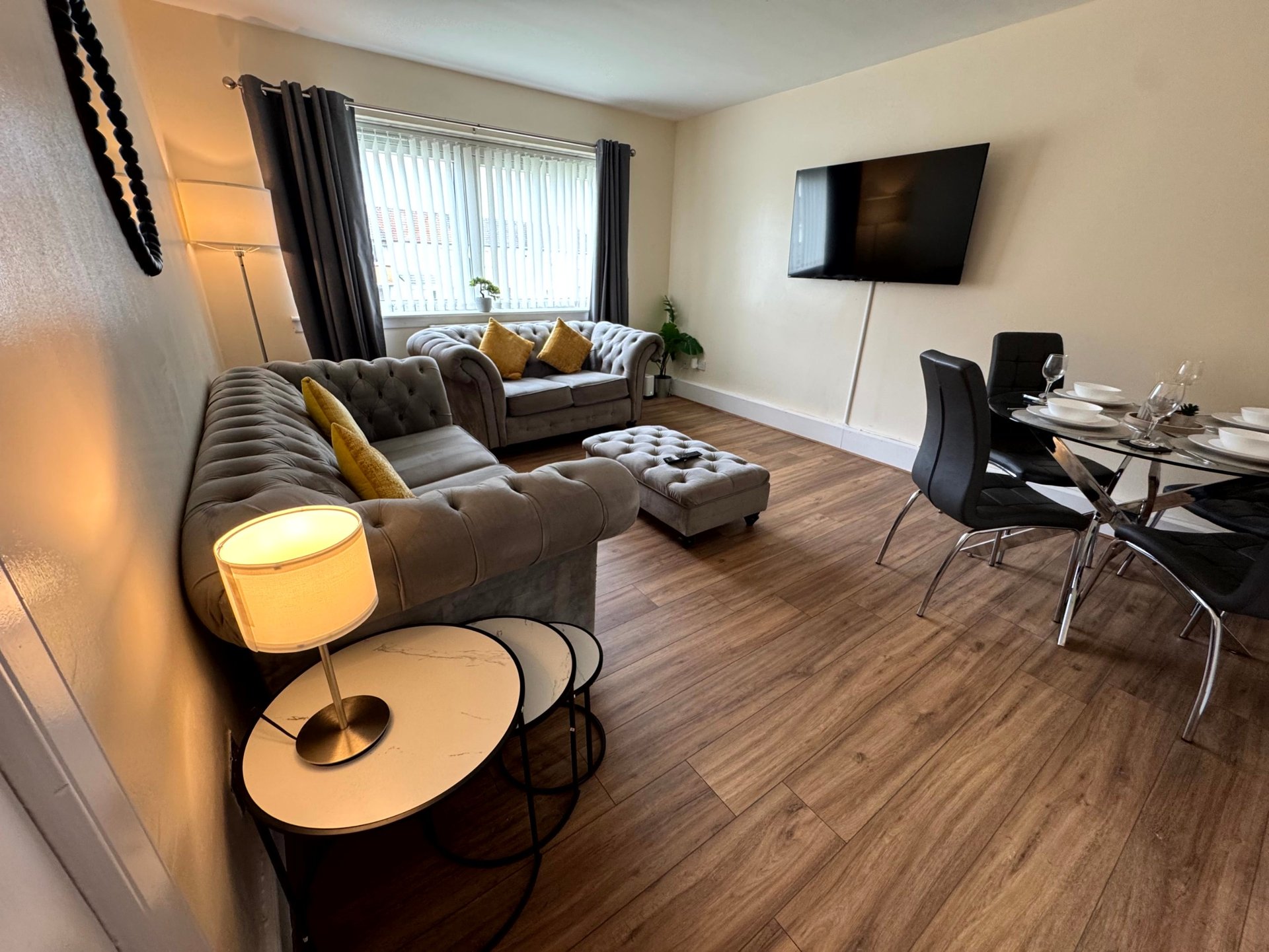 Open-plan living room with brown sectional sofa, wooden flooring, wall-mounted TV and dining area