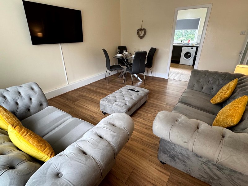 Open-plan living room with grey sofa, wooden floor, TV, dining table and yellow cushions