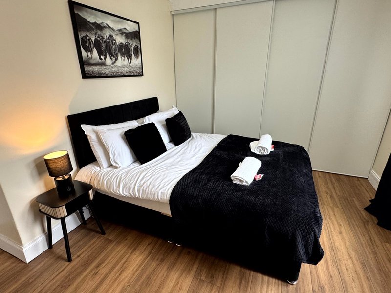 Modern bedroom with black bed, white pillows, bedside lamp, framed wall art and wooden flooring