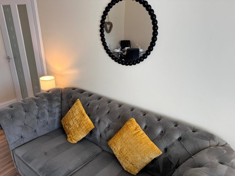 Gray tufted sofa with yellow cushions, round black mirror, and table lamp