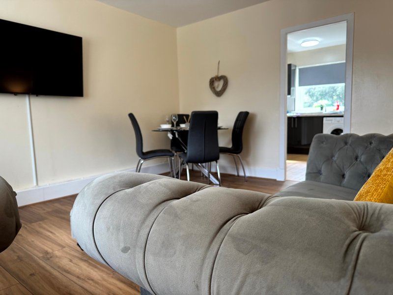 Open-plan living area with grey upholstered sofa, dining table, chairs and wall-mounted TV