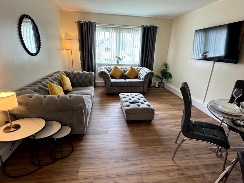 Modern living room with grey sofas, wooden flooring, wall-mounted TV and yellow accent cushions