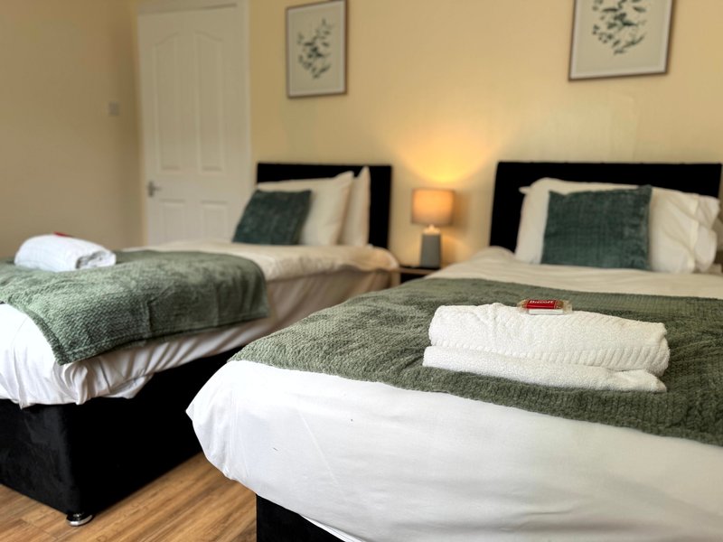 Twin bedroom with two beds, green bedding, wooden floor and framed wall art