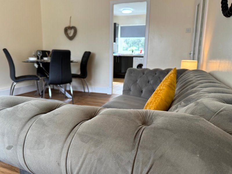 Open-plan living area with upholstered sofa, yellow cushion, dining table and chairs visible beyond