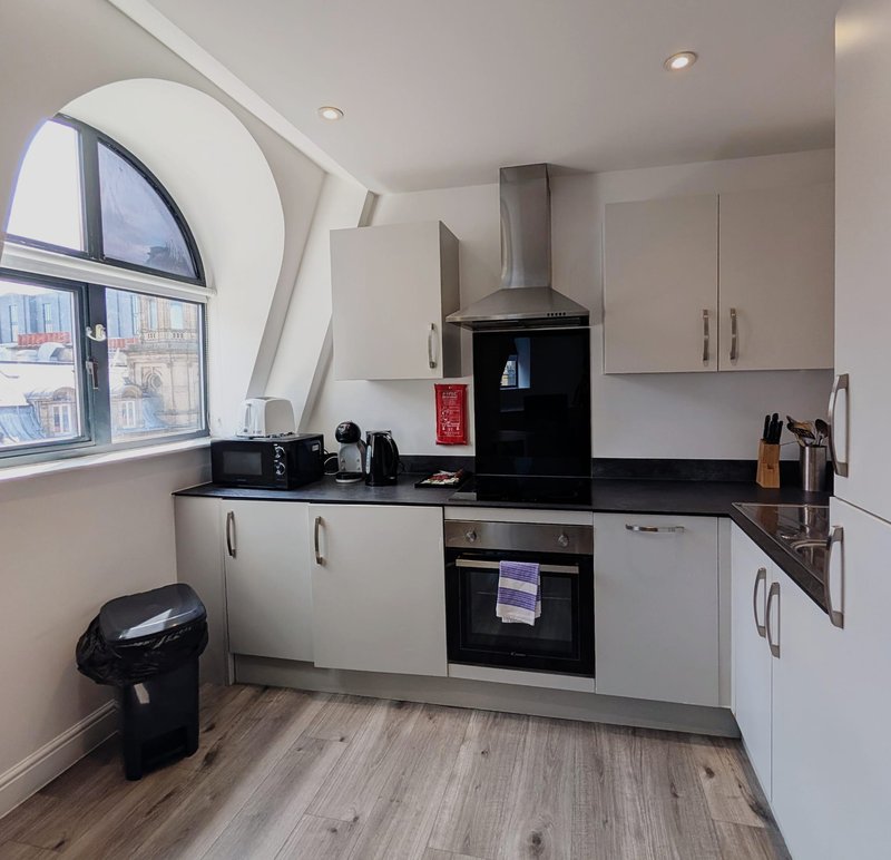 Modern kitchen with white cabinetry, black countertops, stainless steel appliances and curved window