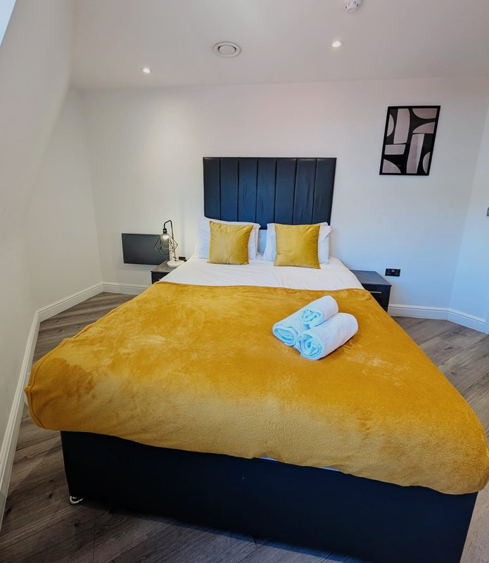 Modern bedroom with double bed, yellow bedding, dark headboard, and rolled towels