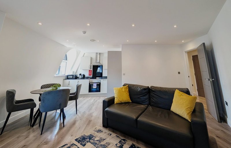 Open-plan living space with black sofa, dining table, kitchen area and wooden flooring
