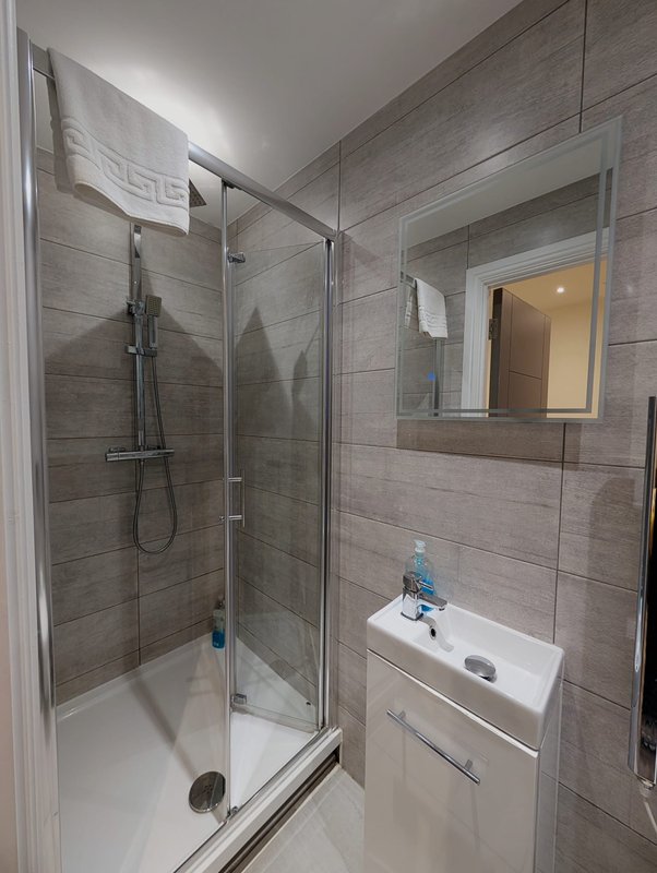 Modern bathroom with walk-in shower, vanity sink, mirror and grey tile walls