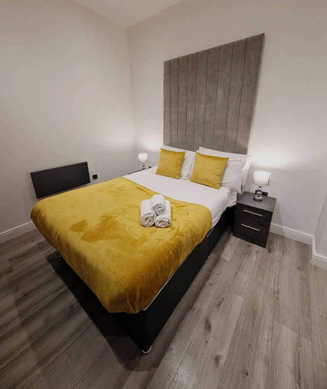 Modern bedroom with double bed, yellow bedding, grey headboard and bedside tables