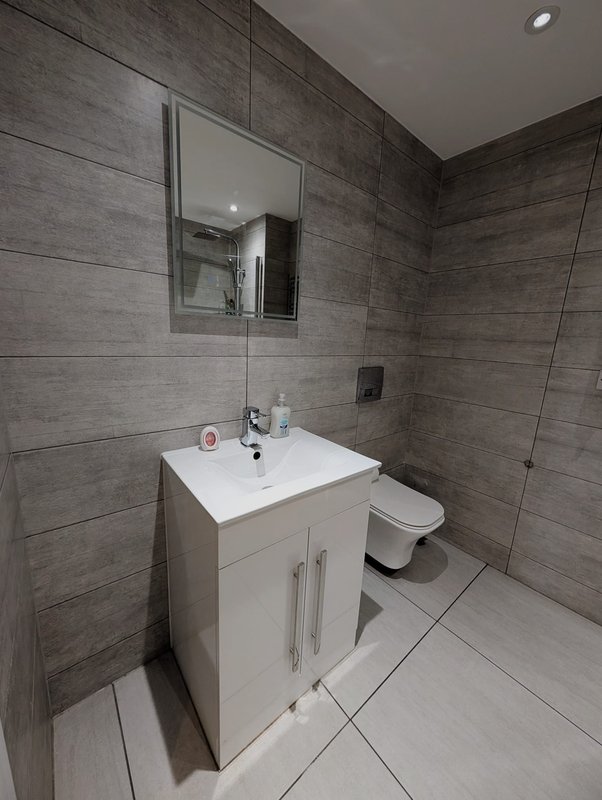 Modern bathroom with white vanity, mirror, toilet, and grey tile walls