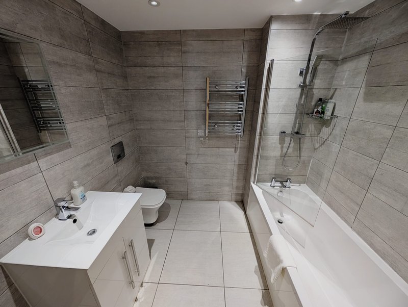 Modern bathroom with grey tile walls, white vanity sink, toilet, and walk-in shower enclosure