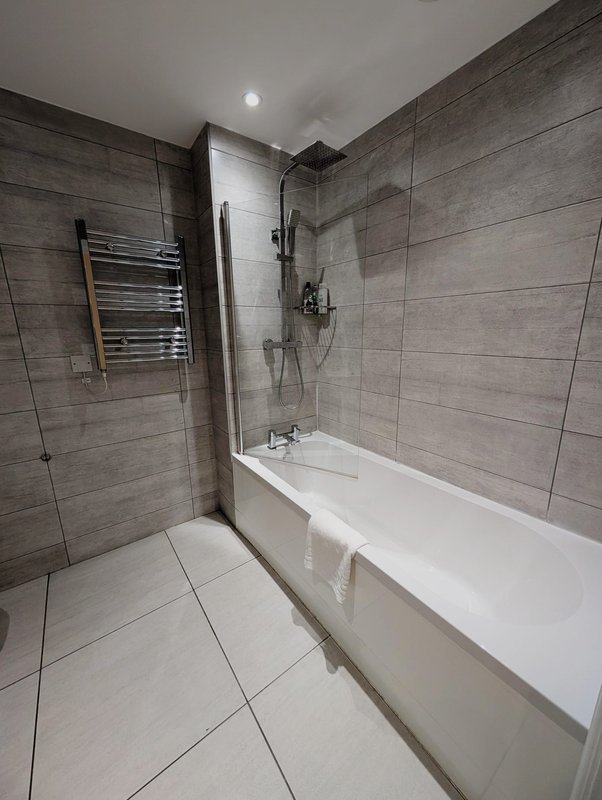 Modern bathroom with grey tile walls, white bathtub, glass shower enclosure and heated towel rail